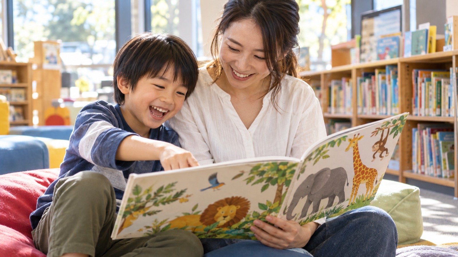 地域の図書館の絵本コーナーで、動物の絵本を一緒に読んで笑う男の子と母