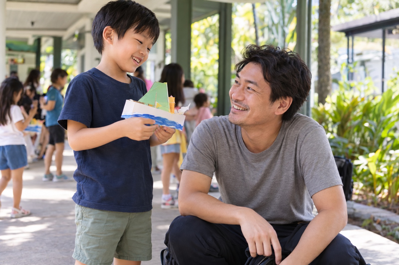 インター校の渡り廊下で、作った工作を見せる男の子と、しゃがんで迎える父親