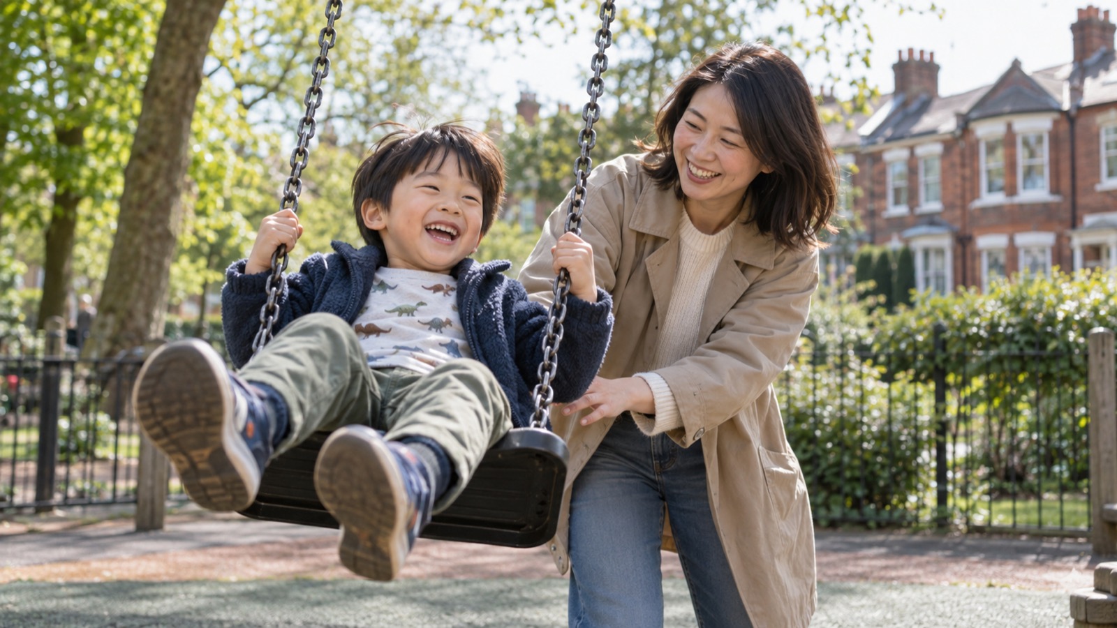 赤レンガの住宅街の公園で、ブランコをこぐ男の子の背中を押す母