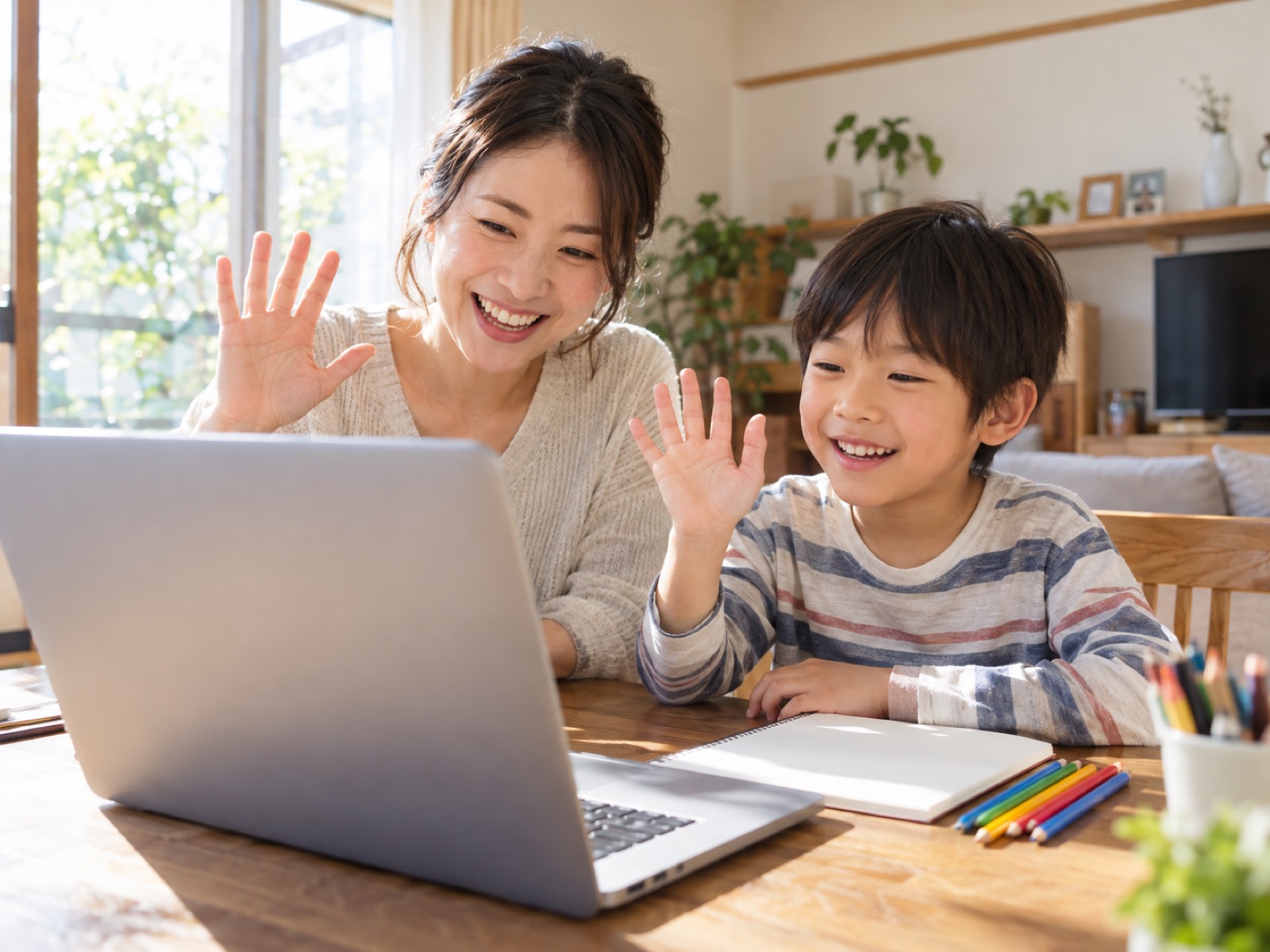 自宅のダイニングで、ノートパソコンのオンライン英会話に笑顔で手を振る母と男の子