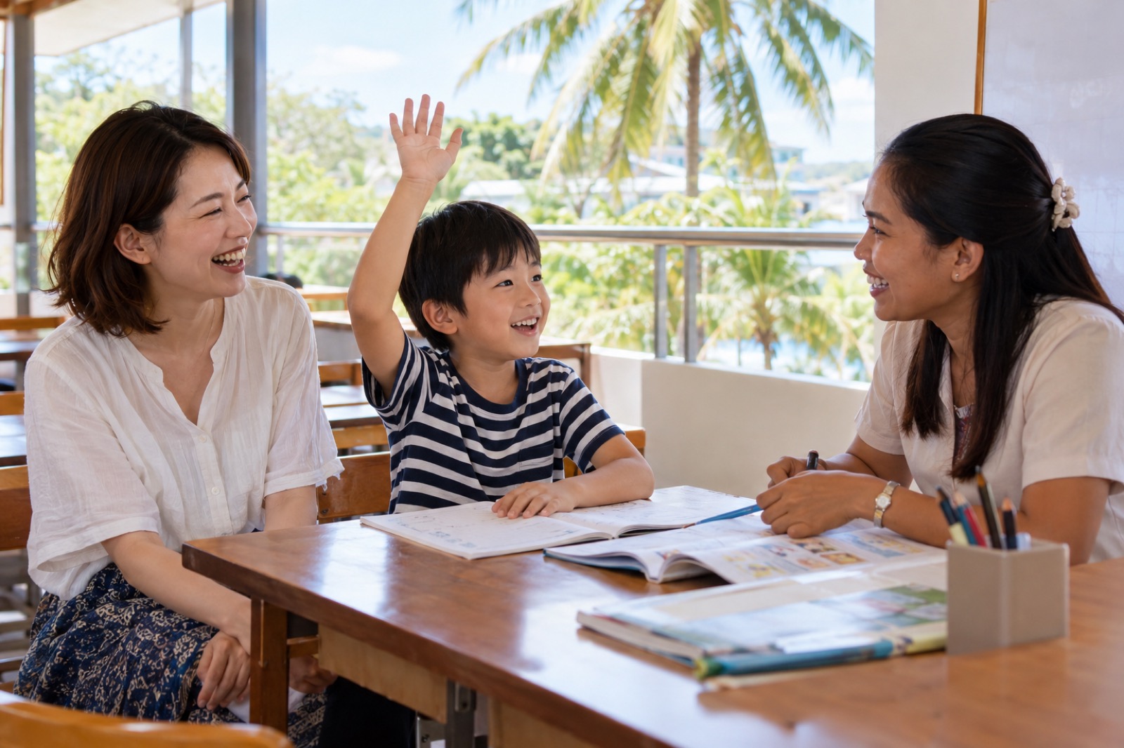 セブの語学学校の明るい教室で、フィリピン人の先生とマンツーマンの授業を受け、元気よく手を挙げる小2の息子と隣で笑う母